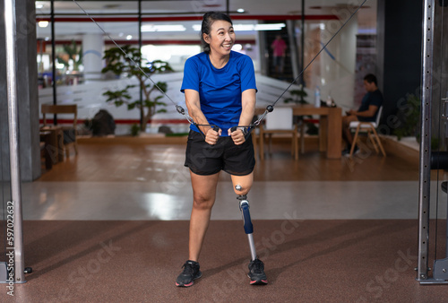 Woman with prosthetic leg exercising on multistation at gym for arm and shoulders muscles