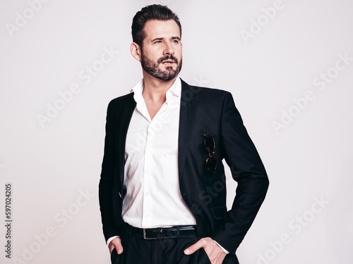 Portrait of handsome confident stylish hipster lambersexual model. Sexy modern man dressed in black elegant suit. Fashion male posing in studio, isolated on white