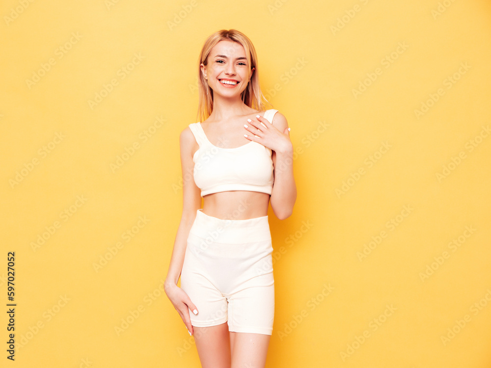 Young beautiful smiling blond female in summer cycling shorts clothes. Sexy carefree woman posing near yellow wall in studio. Positive model having fun indoors. Cheerful and happy Young beautiful smiling blond female in summer cycling shorts clothes. Sexy carefree woman posing near yellow wall in studio. Positive model having fun indoors. Cheerful and happy