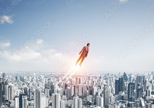 Businessman in suit and aviator hat flying in sky