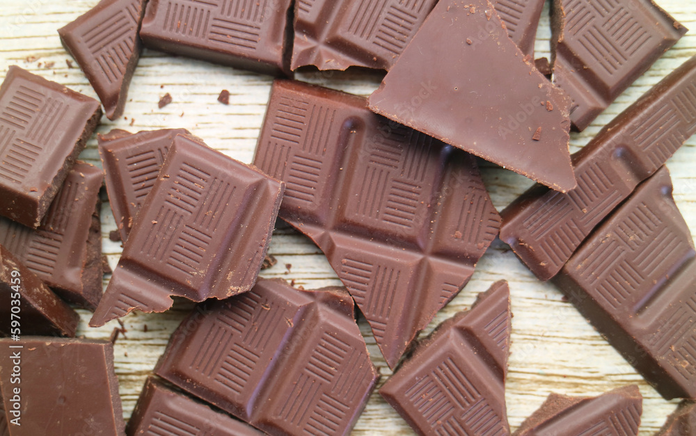 Heap of cracked dark chocolate bars scattered on wooden background Heap of cracked dark chocolate bars scattered on wooden background