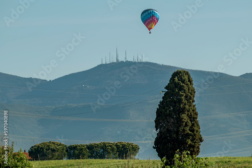 A colorful hot air balloon flies over the Tuscan countryside with Monte Serra in the background, Pisa, Italy