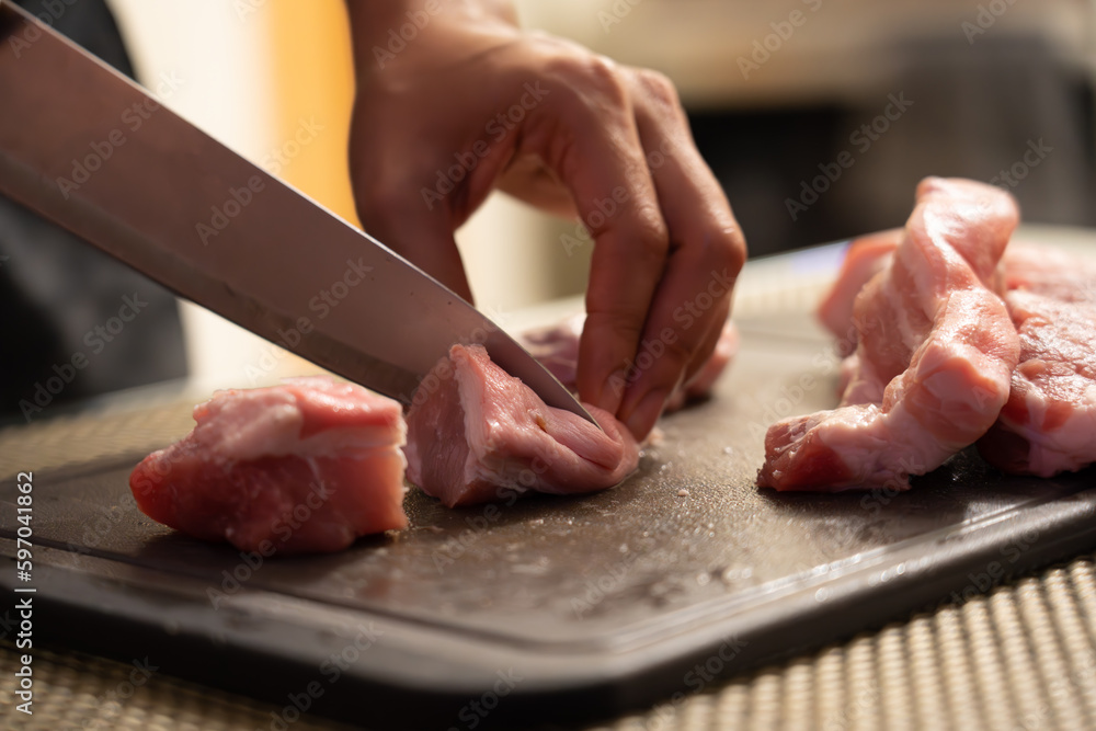 Close up of woman cutting raw pork slices on a grey cutting board