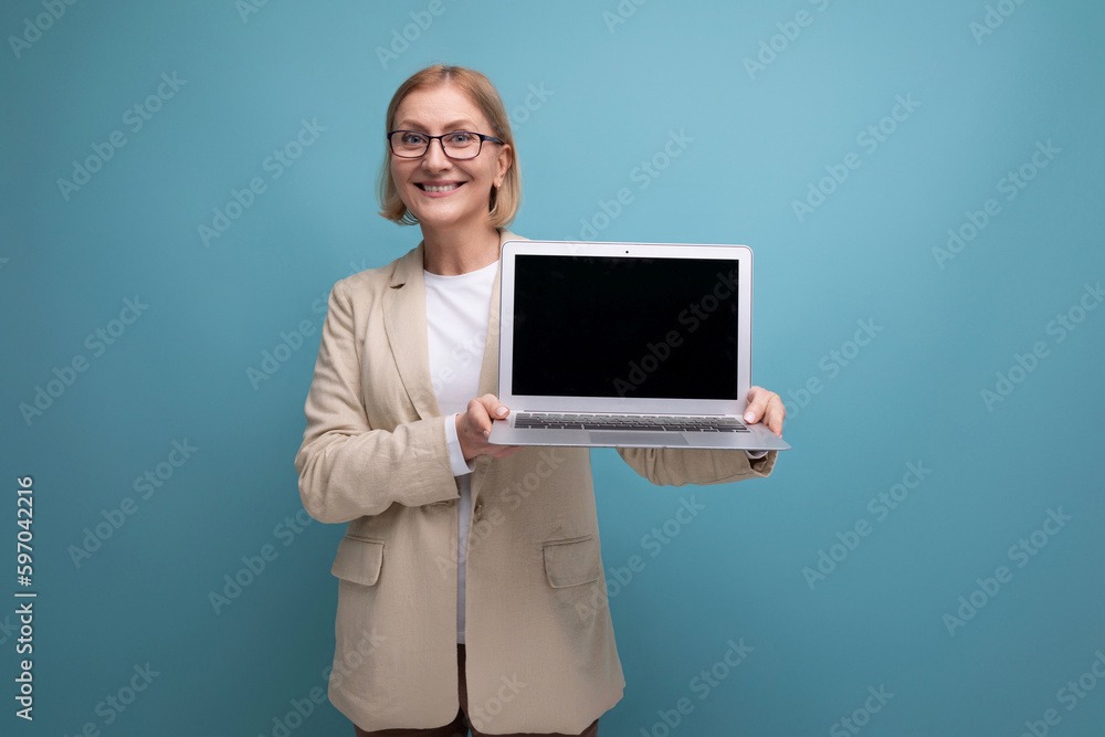 middle-aged mature woman in jacket masters new technique using laptop on studio background with copy space middle-aged mature woman in jacket masters new technique using laptop on studio background with copy space