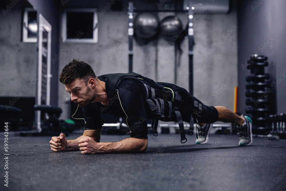 Full body burning exercise, using new EMS technology. A young attractive man in clothes for EMS is in a plank position on elbows in the gym. Electrical muscle stimulation Full body burning exercise, using new EMS technology. A young attractive man in clothes for EMS is in a plank position on elbows in the gym. Electrical muscle stimulation