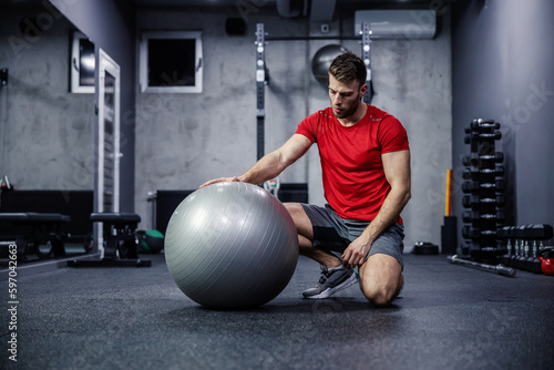 Mental preparation for strong physical functional training. A good looking man in sportswear touches a fitness ball and sets up to perform exercises. Concentration for success in exercises