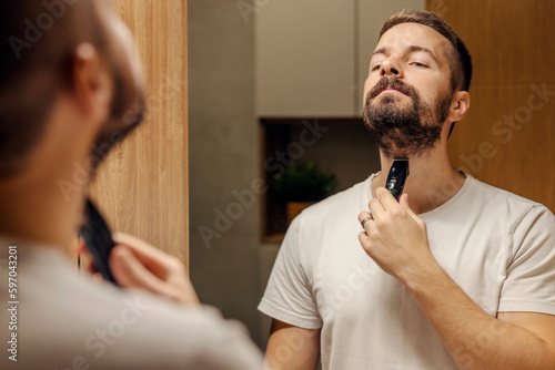 Foto Reflection of a man trimming his beard in a bathroom in front of the mirror