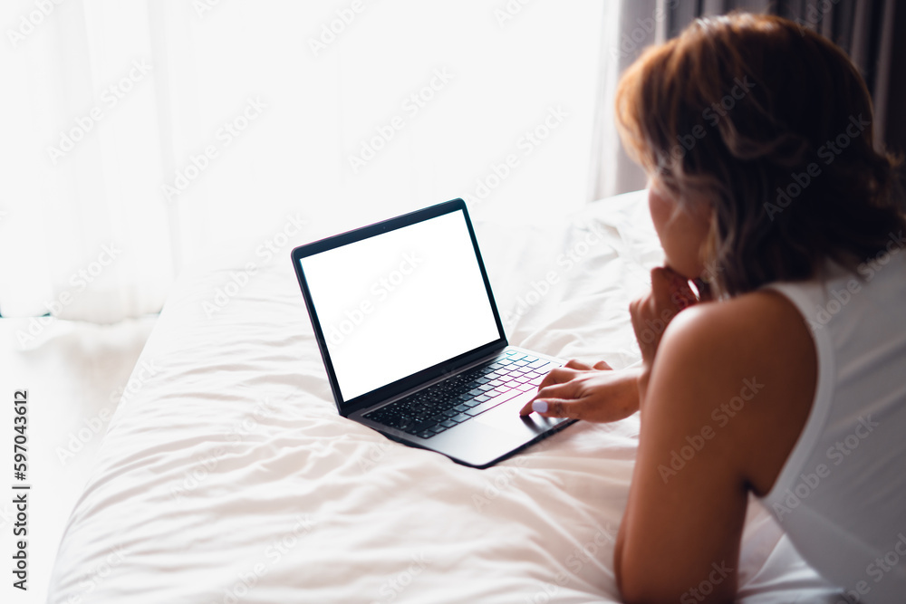Fototapeta premium Laptop on empty bed,Caucasian woman laying on bed using laptop