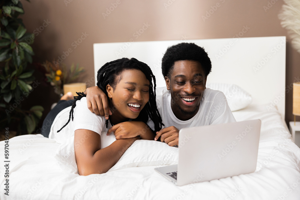 Young african american black couple lying on bed in front of laptop ...