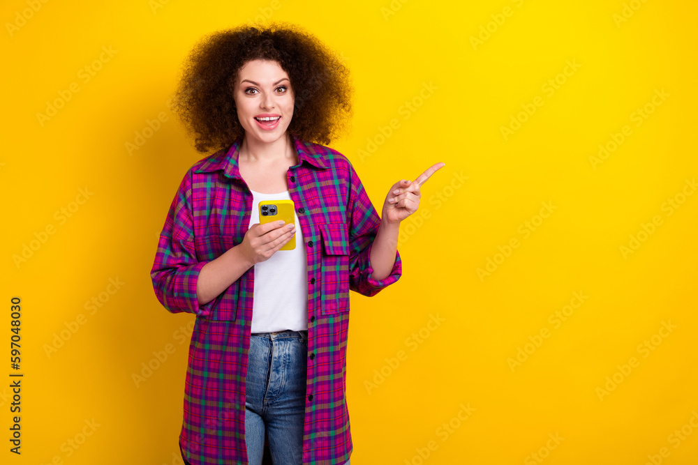 Photo of surprised young woman wear magenta checkered shirt hold smartphone direct finger mockup download app isolated on yellow color background Photo of surprised young woman wear magenta checkered shirt hold smartphone direct finger mockup download app isolated on yellow color background