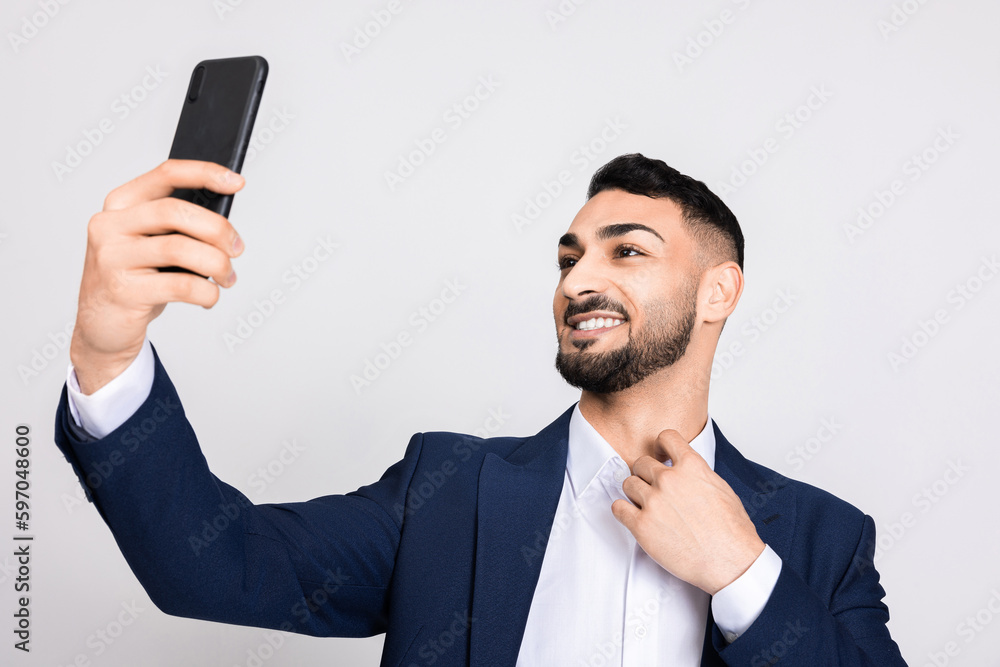 Happy delighted turkish indian middle eastern man guy buisnessman in ellegant suit holding modern new cellphone in hands taking picture selfie speaking with family wife via video link chat time. Happy delighted turkish indian middle eastern man guy buisnessman in ellegant suit holding modern new cellphone in hands taking picture selfie speaking with family wife via video link chat time.