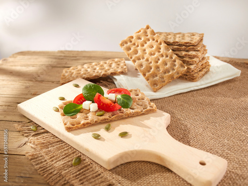 brown crispbreads with tomatoes and cheese on a wooden board. healthy snack with cereal bread. breakfast on a sunny day. crispy bread stuffed with vegetables
