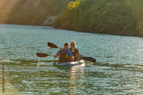 A young couple enjoying an idyllic kayak ride in the middle of a beautiful river surrounded by forest greenery in sunset time 