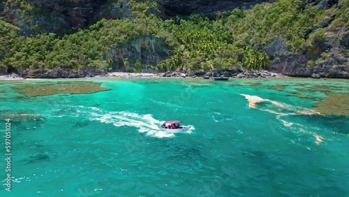 Tourist boat sailing in turquoise sea waters of Playa Fronton beach, Samana in Dominican Republic. Aerial backward