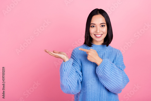 Photo of positive cute girl toothy smile indicate finger arm hold empty space isolated on pink color background