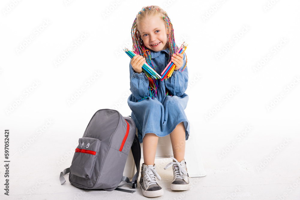 Fulllength photo of beautiful adorable little pupil sitting on white floor isolated looking into distance holding colorful pencils in hands showing at camera posing with school equipment. Fulllength photo of beautiful adorable little pupil sitting on white floor isolated looking into distance holding colorful pencils in hands showing at camera posing with school equipment.
