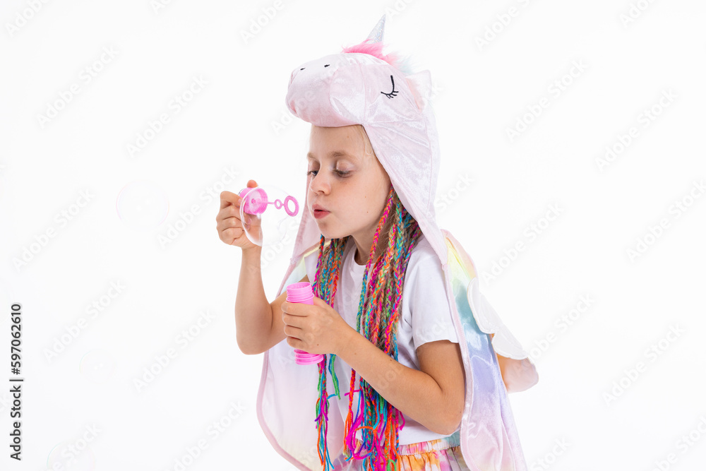 Happy preschooler daughter on white background in studio isolated blowing soap bubbles wearing funny unicorn hat and colorful braids posing for stylish magazine shop. Vacation concept. Happy preschooler daughter on white background in studio isolated blowing soap bubbles wearing funny unicorn hat and colorful braids posing for stylish magazine shop. Vacation concept.