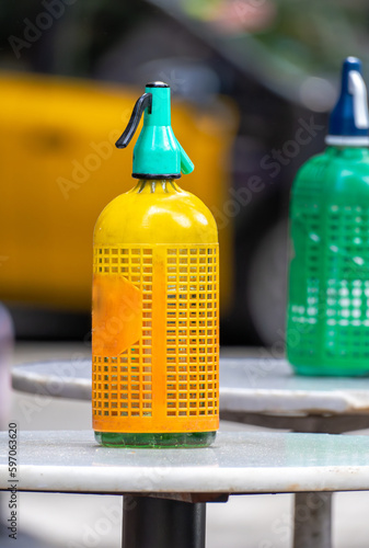Obraz na plátně Plastic mesh siphon in orange yellow and other old and vintage green for soda on top of small round high tables on the terrace of a quaint old bar in Barcelona for vermouth