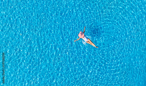 Aerial view with woman in bikini sunbathing as laying on swim ring as blue sea water in background