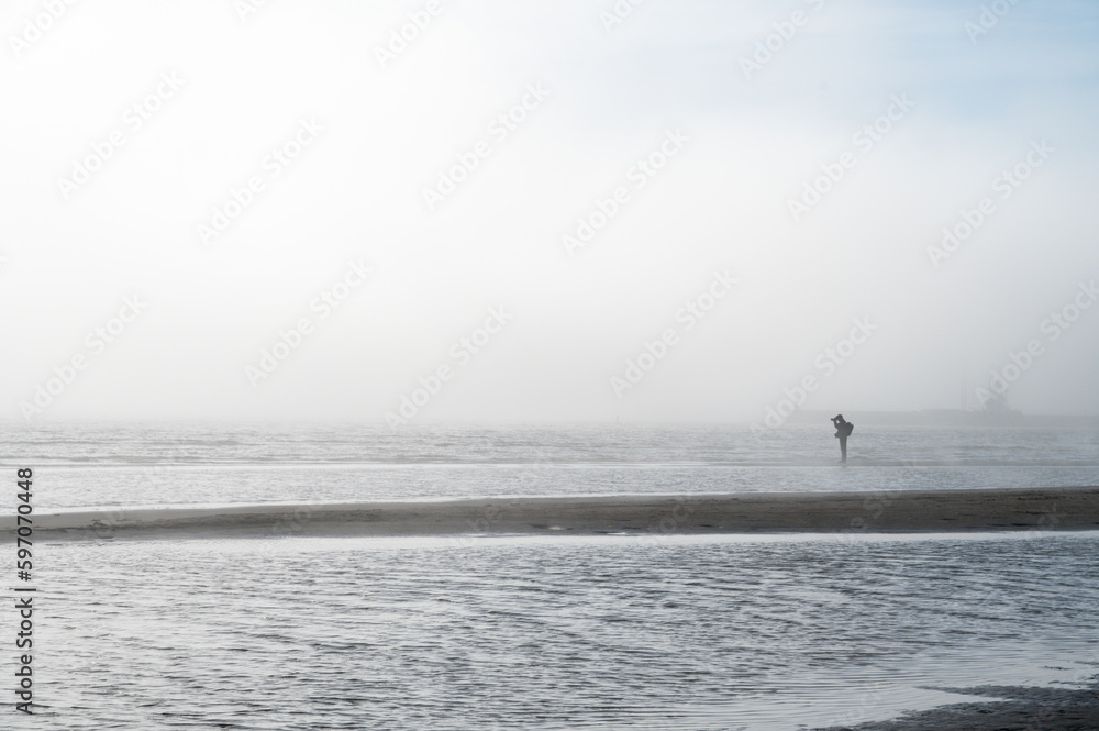 Fog on Baltic sea coastline at spring. Moody weather, mist. Person standing in distance