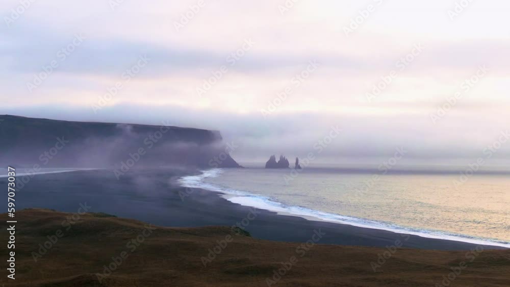 Slow motion drone view of waves gently crashing to the shore amidst an overcast sky with a cliff and rock formations in the background. Slow motion drone view of waves gently crashing to the shore amidst an overcast sky with a cliff and rock formations in the background.