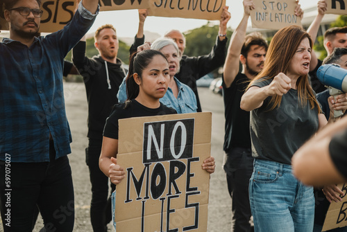 Group of multiethnic protesters in casual clothes with carton placards standing on street and shouting to loudspeaker during riot photo