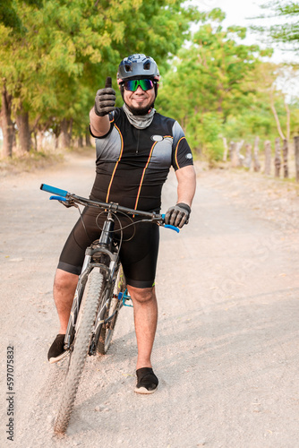 Fototapeta Naklejka Na Ścianę i Meble -  Cyclist giving thumbs up on a road. Professional cyclist doing ok gesture on his bike