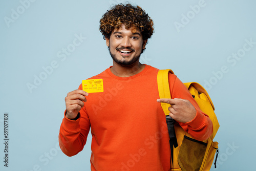 Young fun teen Indian boy student wear casual clothes backpack bag hold in hand point on credit bank card isolated on plain pastel light blue cyan background. High school university college concept.