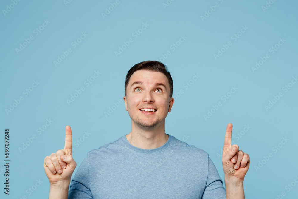 Young happy fun man wear casual t-shirt point index finger overhead indicate on workspace area copy space mock up isolated on plain pastel light blue cyan background studio portrait Lifestyle concept. Young happy fun man wear casual t-shirt point index finger overhead indicate on workspace area copy space mock up isolated on plain pastel light blue cyan background studio portrait Lifestyle concept.