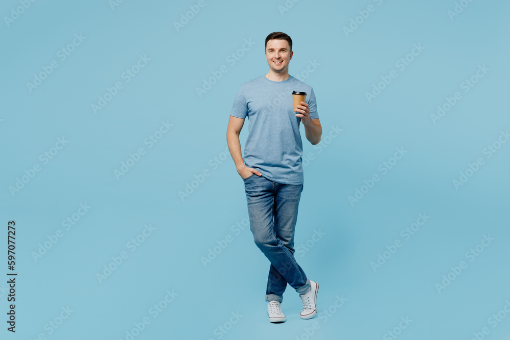 Full body young smiling happy man wear casual t-shirt hold takeaway delivery craft paper brown cup coffee to go isolated on plain pastel light blue cyan background studio portrait. Lifestyle concept.