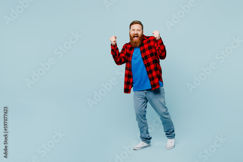 Full body young redhead bearded man he wear casual clothes doing winner gesture celebrate clenching fists say yes isolated on plain pastel light blue cyan background studio portrait Lifestyle concept