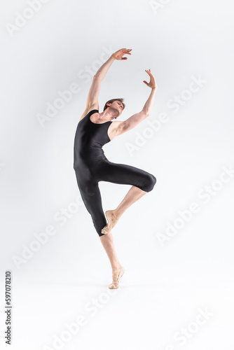 Modern Art Ballet of Young Caucasian Athletic Man in Black Suit Dancing in Studio Over White Background With Lifted Hands.