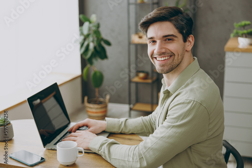 Side view happy young man wear casual clothes sits alone at table in coffee shop cafe restaurant indoors work or study on laptop pc computer browsing internet Freelance mobile office business concept