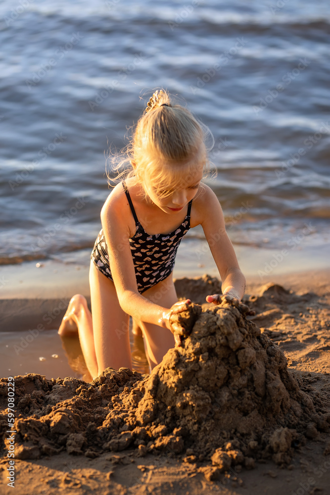 A little girl makes a sand castle on the river bank. A child plays in the sand on the beach. Summer children's games on the sea. A little girl makes a sand castle on the river bank. A child plays in the sand on the beach. Summer children's games on the sea.