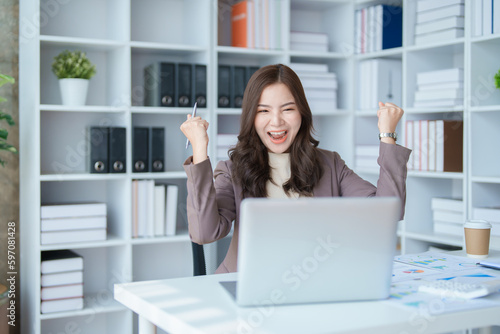 Beautiful young teen asian businesswomen using computer laptop with hands up in winner is gesture, Happy to be successful celebrating achievement success