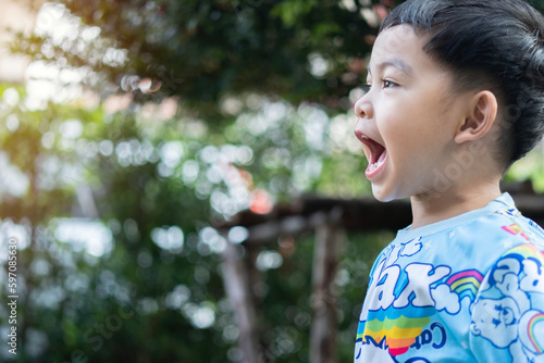 Side view portrait of a little Asian boy shouting with happy wow surprised face over  natural background.