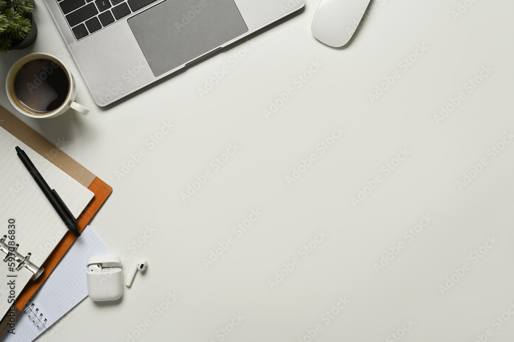 Top view of laptop computer, notepad, cup of coffee and earphone on white working desk Top view of laptop computer, notepad, cup of coffee and earphone on white working desk