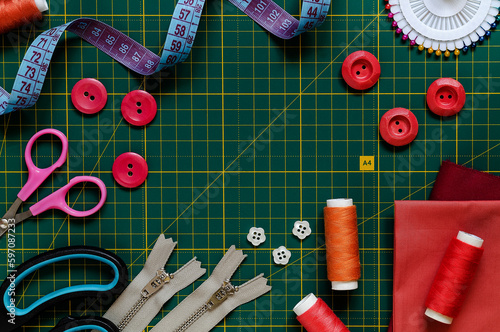 Sewing kit on a green cutting mat. Buttons, threads. cloth, meashuring tape, zippers and scissors. Top view. Copy space.