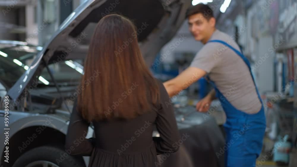 Live camera follows woman walking to man repairing automobile at service station. Back view tracking shot of Caucasian female client approaching to male mechanic fixing vehicle breakage. Slow motion Live camera follows woman walking to man repairing automobile at service station. Back view tracking shot of Caucasian female client approaching to male mechanic fixing vehicle breakage. Slow motion