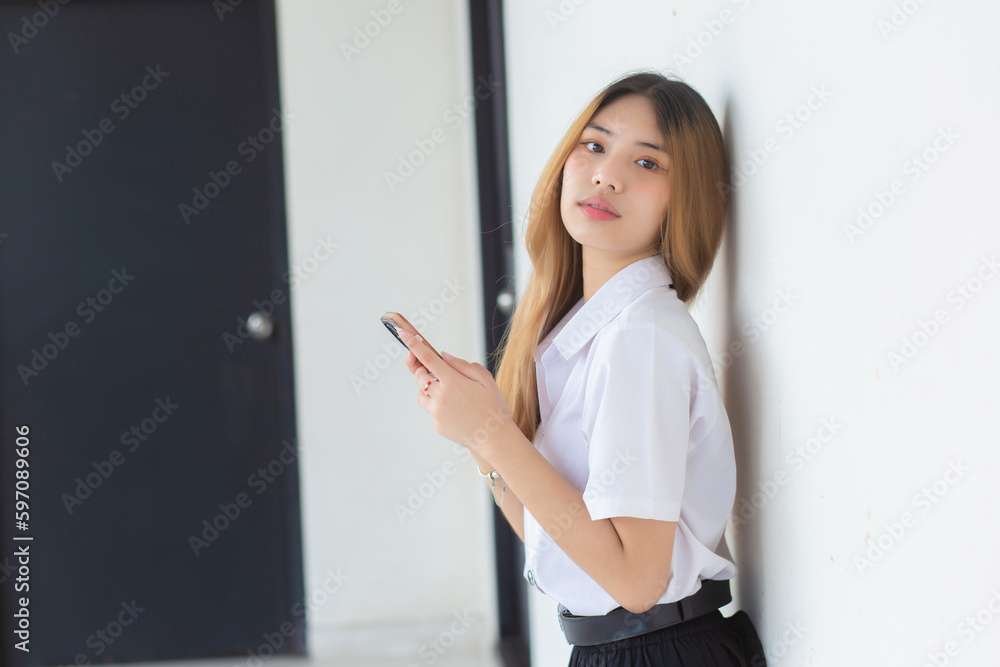 Portrait of cute Asian Thai girl student in a uniform is smiling happily while using a smartphone at university. Portrait of cute Asian Thai girl student in a uniform is smiling happily while using a smartphone at university.