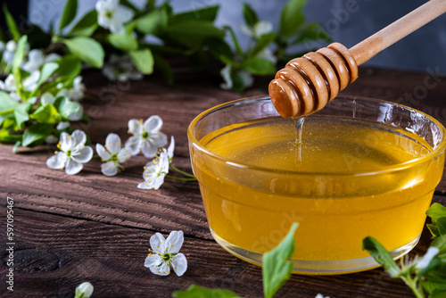 Golden honey in a glass bowl on a wooden table. Fresh honey on the table with spring white fruit tree flowers. Wooden spoon with honey on the background of flowering fruit branches.