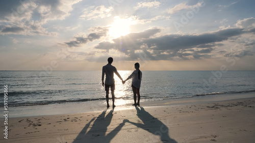 Happy Romantic Young couple holding hands Enjoying Beautiful Sunset on the Beach. Travel Vacation