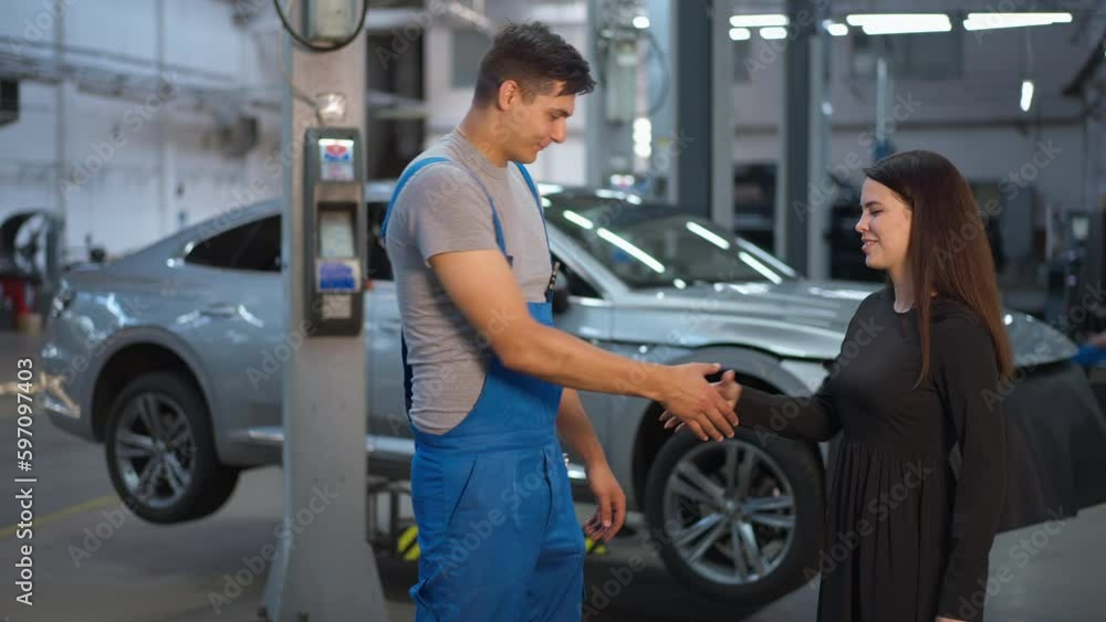 Side view portrait of expert maintenance engineer talking with client shaking hands leaving in slow motion. Caucasian professional man with young woman in auto service station indoors Side view portrait of expert maintenance engineer talking with client shaking hands leaving in slow motion. Caucasian professional man with young woman in auto service station indoors