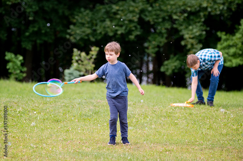 Summer holidays. Schools out. Two brothers playing with soap bubbles in the park. Cheerful happy family having a picnic. Vacations and trips out of town in nature.
