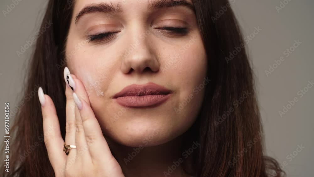 A brunette woman puts cream on her face and begins to rub it with circular movements. Young woman applying moisturizer to her face for skin care. A brunette woman puts cream on her face and begins to rub it with circular movements. Young woman applying moisturizer to her face for skin care.