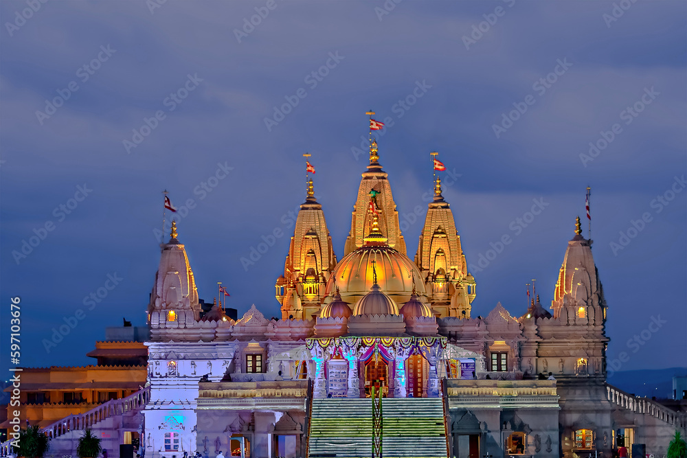 Night illuminated Shree Swaminarayan temple with dark blue cloud background.