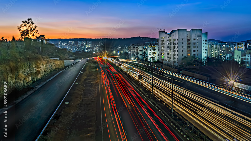 Slow shutter speed image of light trails, beautiful sunset sky , buildings and flowing traffic on motorway.
