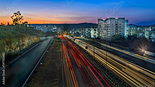 Slow shutter speed image of light trails  beautiful sunset sky   buildings and flowing traffic on motorway.