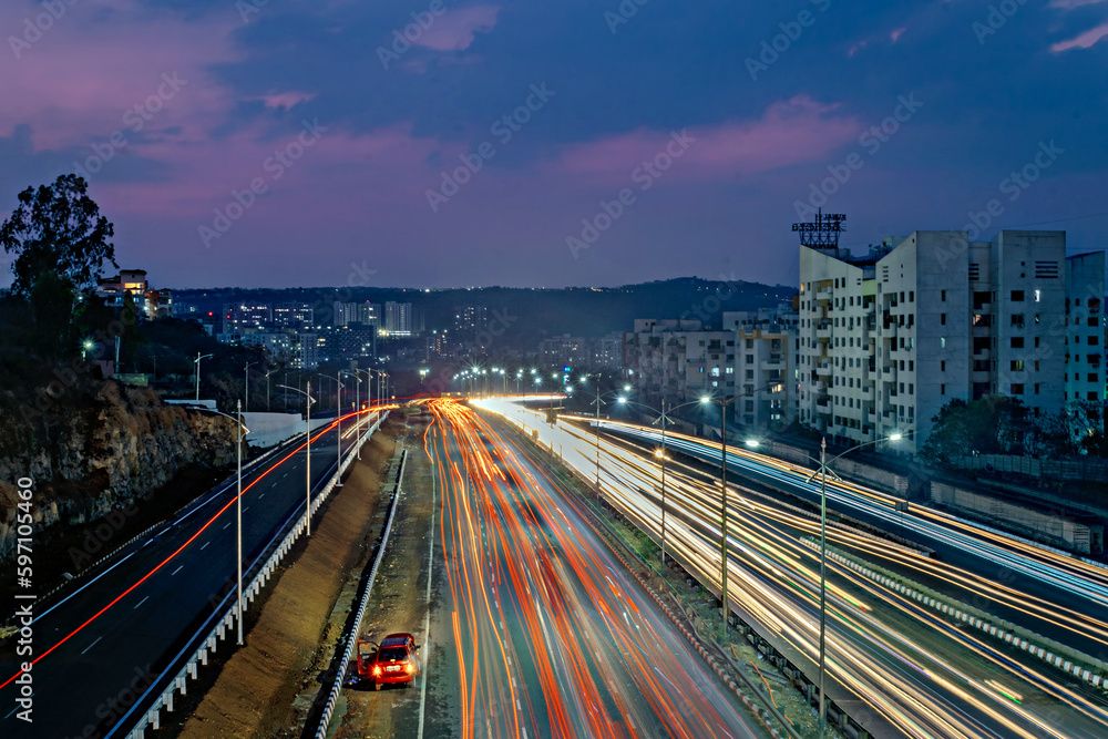 Fototapeta premium Slow shutter speed image of light trails, beautiful sunset sky , buildings and flowing traffic on motorway.