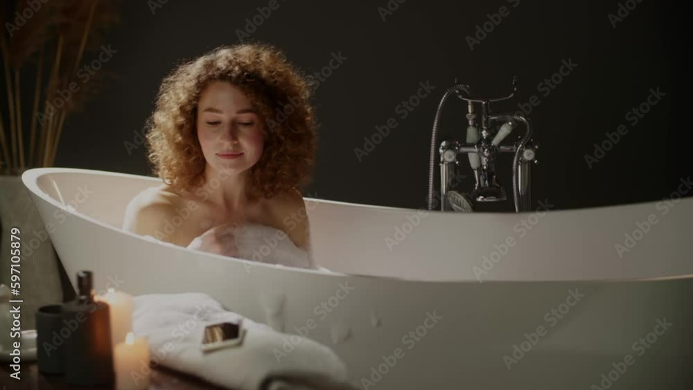 A beautiful woman sits in the bath and picks up her phone to read the notification, but drops it into the water. A woman with curly hair is wiping a phone that she dropped into the water with a towel. A beautiful woman sits in the bath and picks up her phone to read the notification, but drops it into the water. A woman with curly hair is wiping a phone that she dropped into the water with a towel.